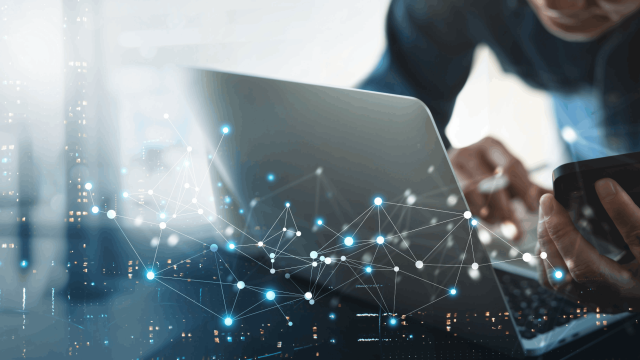 Profesional usando portátil y móvil con red digital simbolizando la conectividad y la transformación digital en la empresa.